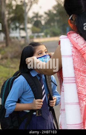 Ein indisches Schulkind, das nach einer Pandemie wieder zur Schule geht, wobei ihre Mutter Nasenmaskenschutz trägt Stockfoto