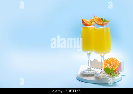 Klassischer Sommer-Mimosas-Cocktail mit Orangensaft auf hellblauem Hintergrund. Sommerliches Bar-Menü mit Kopierbereich Stockfoto