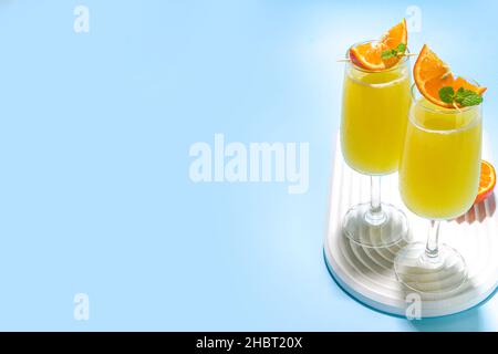 Klassischer Sommer-Mimosas-Cocktail mit Orangensaft auf hellblauem Hintergrund. Sommerliches Bar-Menü mit Kopierbereich Stockfoto