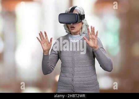 Betäubt ältere Frau mit Virtual-Reality-Headset auf abstraktem Bokeh-Hintergrund. Stockfoto