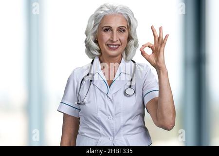 Leitende Ärztin zeigt das Symbol OK, das auf unscharfem Hintergrund posiert. Stockfoto