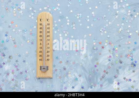 Thermometer zeigt niedrige plus Temperatur und Konfetti Dekoration auf weiß und blau mit Sternen festlichen Hintergrund. Weihnachtliches Wetterkonzept, Platz zum Kopieren Stockfoto