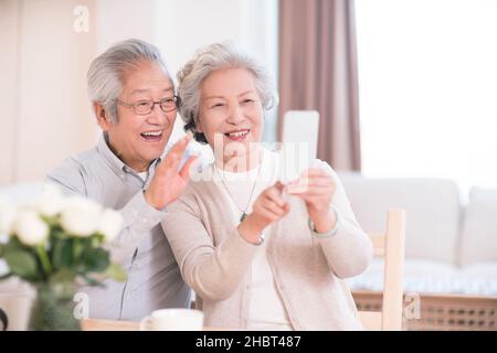 Ein älteres Paar, das zu Hause ein Mobiltelefon benutzt, um Selfies zu machen Stockfoto