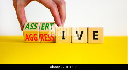 Aggressives oder durchsetzungskräftiger Symbol. Geschäftsmann dreht Holzwürfel, ändert das Wort aggressiv zu durchsetzungsfähig. Schöner weißer Hintergrund, Kopierbereich. Busi Stockfoto