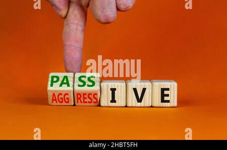 Passives oder aggressives Symbol. Geschäftsmann dreht Holzwürfel und ändert das Wort passiv in aggressiv. Schöner orangefarbener Hintergrund, Kopierbereich. Busi Stockfoto