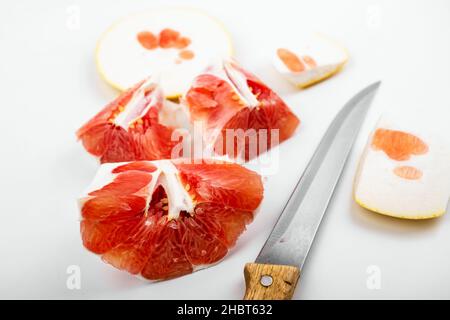 Stücke und Schale von roter Grapefruit, schöne Textur und Struktur von Fruchtfleisch, Messer auf weißem Hintergrund, Nahaufnahme. Stockfoto