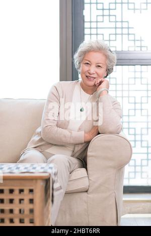Glückliche alte Frau, die auf dem Sofa sitzt Stockfoto