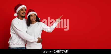 Liebevolles afroamerikanisches Paar in Weihnachtsmützen, das Platz für Kopien zeigt Stockfoto