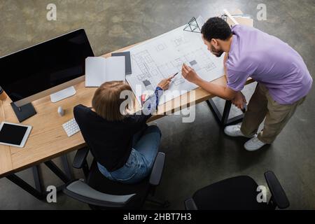 Draufsicht auf multiethnische Innenarchitekten, die Blaupause in der Nähe von Farbmustern diskutieren Stockfoto
