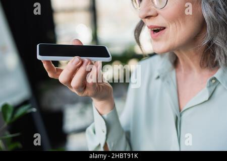 Beschnittene Ansicht einer grauhaarigen Geschäftsfrau, die im Büro Sprachnachrichten auf dem Mobiltelefon aufzeichnet Stockfoto