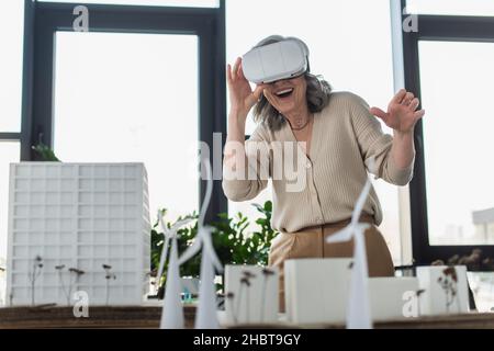 Geschäftsfrau, die ein vr-Headset in der Nähe verschwommener Modelle von Bürogebäude verwendet Stockfoto
