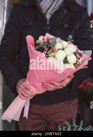 Junger Mann mit einem schönen Blumenstrauß aus der Nähe. Mann mit warmer Jacke und Schal. Nicht erkennbare Menschen. Vertikal zugeschnittenes Foto, Stockfoto