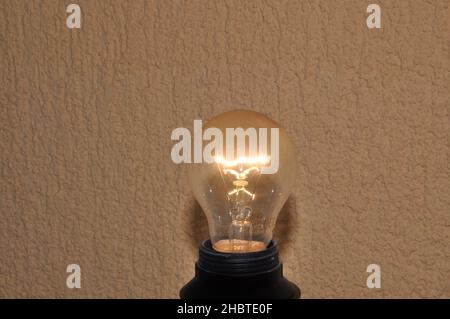 Glühbirne auf rauem beigen Hintergrund, Konzept der Kreativität. Stockfoto