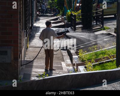 Medellin, Kolumbien - August 2 2021: Die alte lateinische Dame bewässert kleine Parzellen von Grüngras bei ihrem Haus Stockfoto