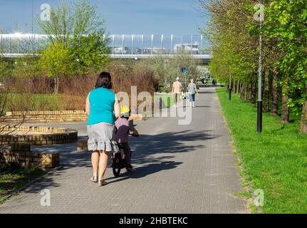 POZNAN, POLEN - 22. Apr 2018: Eine Rückansicht einer Mutter, die ihrem Kind beibringt, an einem sonnigen Tag im Rataje-Park Fahrrad zu fahren Stockfoto