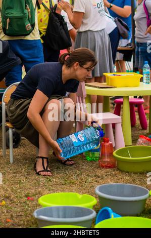 POZNAN, POLEN - 09. Jun 2018: Eine Frau füllt einen Behälter mit Wasser, damit Kinder bei der Feuerwehr mit Wasserpistolen spielen können Stockfoto