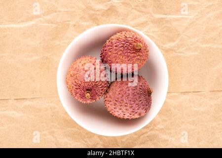 Mehrere geschälte reife süße Litchi-Früchte in einer weißen Untertasse auf Bastelpapier, Nahaufnahme, Draufsicht. Stockfoto