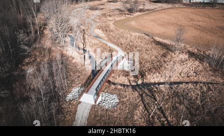 Luftaufnahme über Wanderwegebrücke im Herbst. Unter der Fußgängerbrücke fließt ein kleiner, kurvender Bach. Stockfoto