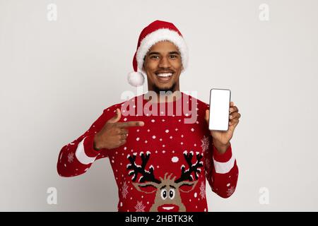 Lächelnder schwarzer Mann im weihnachtsmann-Hut zeigt auf das Smartphone Stockfoto