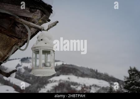 Weißer Kronleuchter, der im Winter mit Schnee an einem Holzhaus in der schweiz hängt Stockfoto