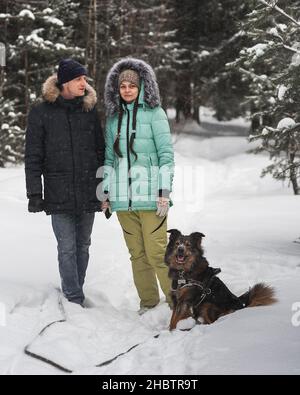 Nettes junges Paar, das Spaß mit ihrem Hund im Winterwald hat Stockfoto