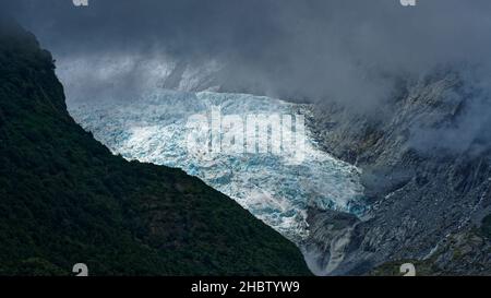 Franz Josef Gletscher unter stürmischem Himmel, Westland Tai Poutini Nationalpark Südinsel, Westküste, Neuseeland. Schmelzwasser, das ins Tal fließt Stockfoto