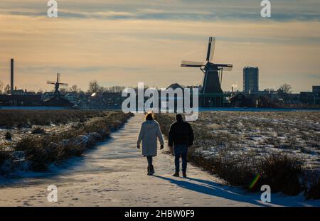 Die Menschen genießen einen Spaziergang auf einem gefrorenen Kanal um historische holländische Windmühlen in Zaanse Schans im Winter Stockfoto