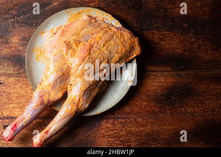 Rohe Lammkeule mit Gewürzen, gekocht zum Kochen auf einem Teller auf einem Holzboden. Stockfoto