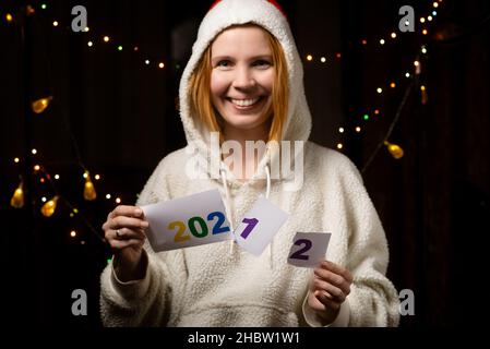 2021 zu 2022 wird von einer lächelnden Frau in einem Neujahrshut geändert. Stockfoto