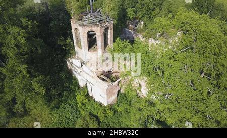 Wunderschöne Details einer verlassenen Kirche, die an einem sonnigen Tag im Sommerwald zurückgelassen wurde. Luftaufnahme des Ivy-Wachstums auf Bauruinen unter grünen Bäumen. Stockfoto