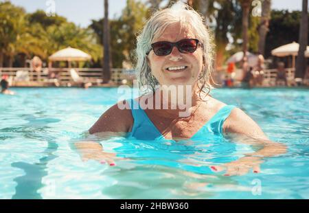 Ältere Frau mit grauen Haaren, in blauem Badeanzug, lächelnd im Hotelpool Stockfoto