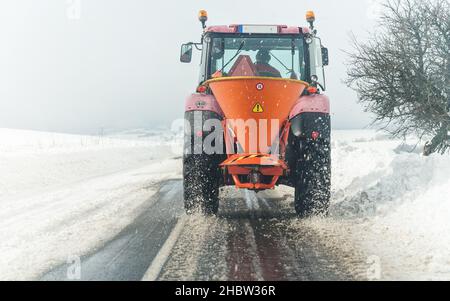 Kleiner Streuwagen-Wartungstraktor, der Eisensalz auf Asphaltstraße verteilt, Blick vom Auto, das dahinter fährt Stockfoto