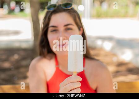 Eine junge lächelnde Frau, die ein Eis-Eis im Park hält Stockfoto