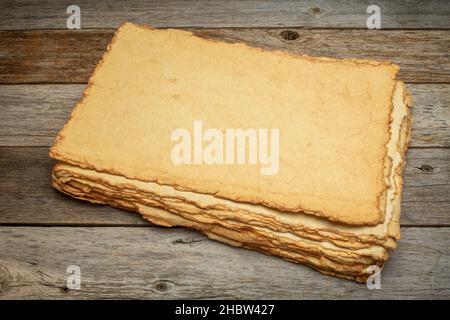 Stapel von leerem handgemachtem Papier mit rauen Kanten gegen rustikales verwittertes Holz Stockfoto