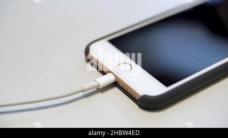 Nahaufnahme des Apple iphone mit dem Ladekabel auf dem weißen Tisch. Ladevorgang eines modernen Geräts, das an ein usb-Kabel angeschlossen ist. Stockfoto