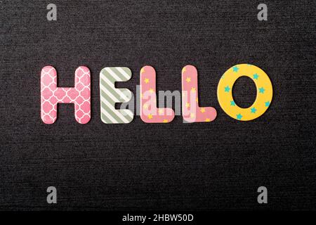 Karte mit Hello-Wort aus bunt gemischten Holzbuchstaben auf einem strukturierten dunkelschwarzen Textilmaterial, das als Nachricht verwendet werden kann Stockfoto