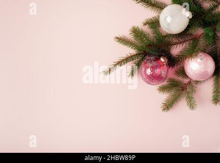 Weihnachtlicher Rahmen aus verzierten Tannenzweigen mit weißen und rosa Glaskugeln auf pastellrosa Hintergrund. Flach liegend. Speicherplatz kopieren. Stockfoto