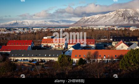 Reykjavik, Island - 24. Januar 2021: Vororte von Reykjavik im Winter, von einem Hügel aus gesehen. Wohngebäude, Mount Esja mit Schnee bedeckt. Stockfoto