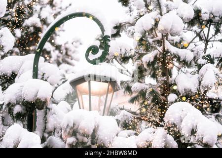 Schöne glühende Straßenlaterne, umgeben von verschneiten Tannen mit Lichtern des traditionellen Weihnachtsfestes. Urlaubskonzept. Winter Urlaub Saison Hintergrund. Stockfoto