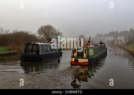 Kanalboote, die im Nebel vorbeifahren. Ein Narrowboat auf dem Weg nach Halsall wird von einem lokalen Ausflugsboot auf dem Leeds und Liverpool Kanal in der Nähe von Burscough passiert. Stockfoto