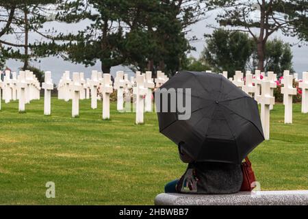 Colleville sur Mer, Frankreich - 5. August 2021: Frau mit schwarzem Regenschirm meditiert auf dem amerikanischen Friedhof, gesäumt von Kreuzen in Corlleville Sur Mer, Stockfoto