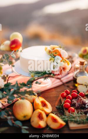 Hochzeitstorte mit Blumen geschmückt steht auf einem Tisch zwischen Obst und Gemüse Stockfoto