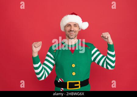 Glücklicher erfolgreicher Mann im Elf Kostüm. weihnachtsmann im weihnachtsmann Hut auf rotem Hintergrund. Stockfoto