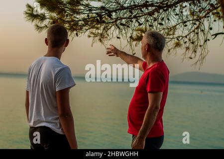 Der Mann zeigt einem Teenager etwas in der Ferne am See Stockfoto
