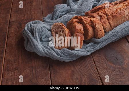 Brotscheiben auf einem Holztisch mit einer grauen Gaze-Tischdecke, frisches Baguette auf einem Holzhintergrund Stockfoto