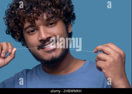 Lächelnder Kerl mit lockigen Haaren, die seine Zähne mit Zahnseide verprügeln Stockfoto
