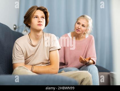 Verärgert und beleidigt Teenager auf dem Sofa sitzen, während Mutter ihn beruhigt Stockfoto