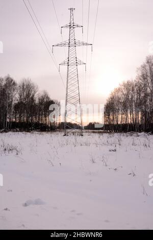 Ein hoher Strommast steht bei Sonnenuntergang in einem mit Schnee bedeckten Feld. Region Nowosibirsk, Sibirien, Russland. Stockfoto