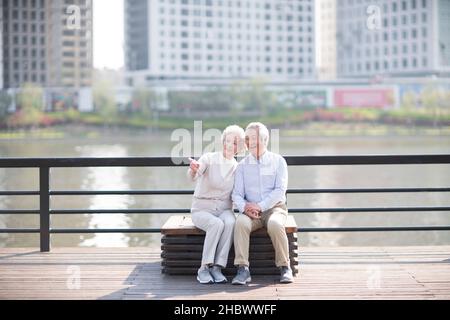Glückliches altes Paar, das am Fluss sitzt, um sich auszuruhen Stockfoto