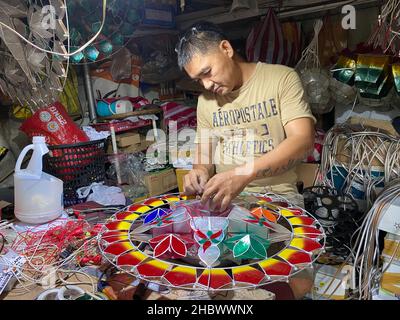 27. November 2021, Philippinen, Elias Aldana: Andrew Flores, 48, fügt einer Bewährung aus Capiz-Muscheln in seinem kleinen Weihnachtsdekor-Laden im Dorf Elias Aldana in Las Pinas City in Metro Manila Glühbirnen hinzu. Im südostasiatischen Inselstaat werden bereits im Mai riesige Mengen sternförmiger Laternen hergestellt. Die Weihnachtsschmuck werden als "Parolen" bezeichnet, und sie existieren nur auf den katholischen Philippinen. Sie werden traditionell aus Bambusstäben und buntem japanischem Papier hergestellt. Heute werden aber auch andere Materialien wie Metalldrähte, Fiberglas und Kunststofffolien verwendet. Foto: Dhang De Stockfoto